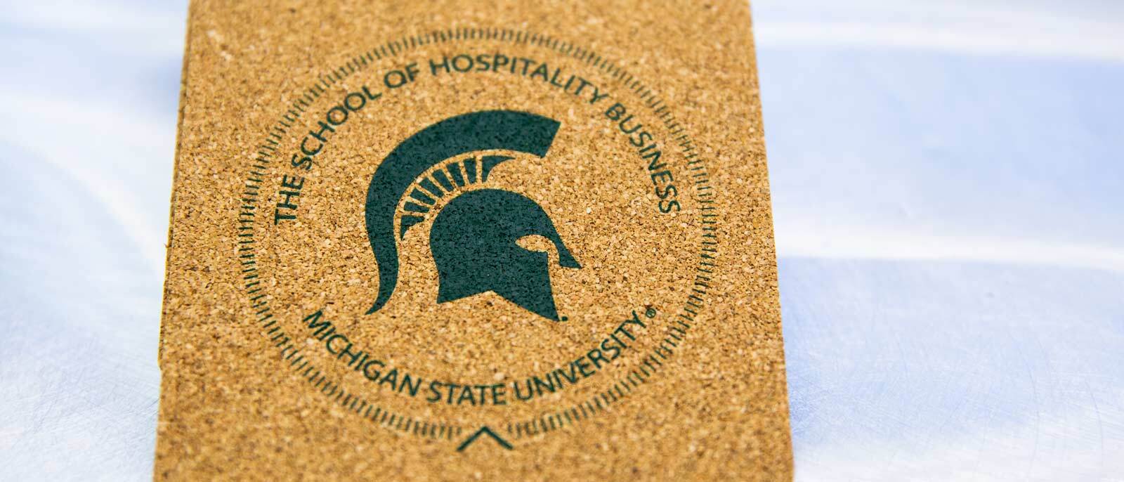A cork coaster with MSU Green imprint of The School of Hospitality Business