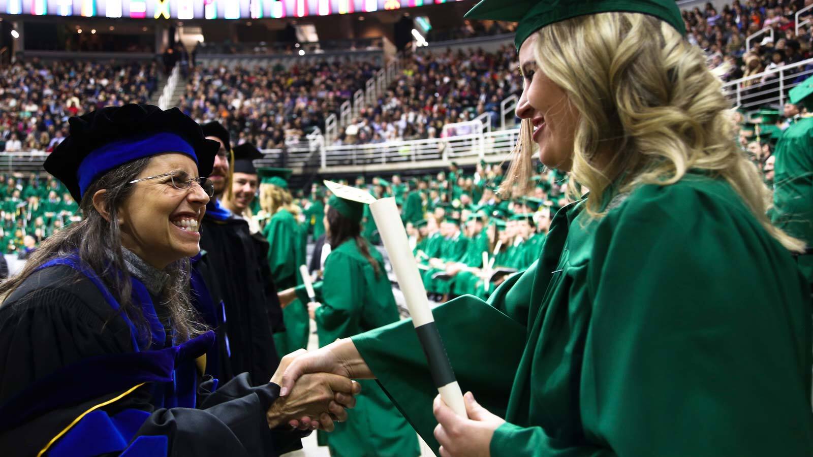 Associate Dean for Undergraduate Programs Kathy Petroni shakes hands with a graduating senior at undergraduate commencement, both dressed in full academic regalia.