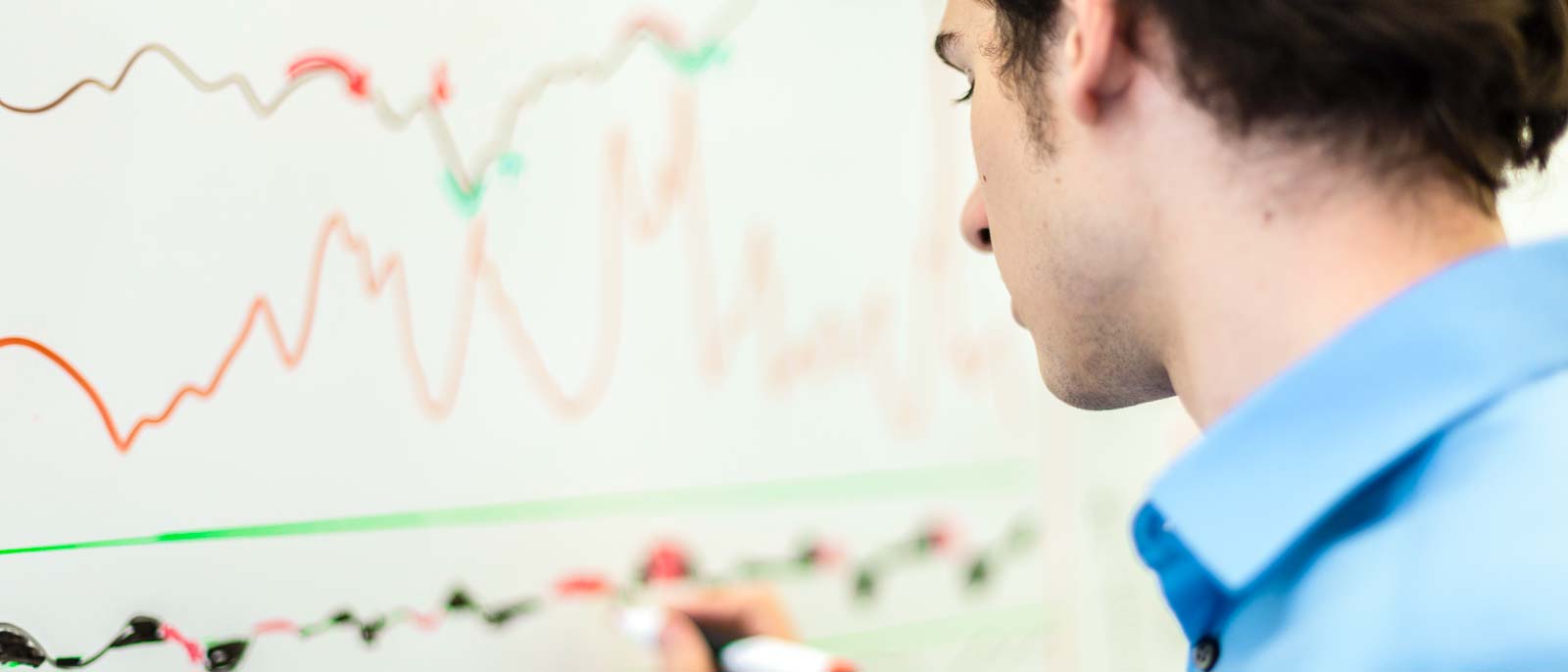 Finance graduate makes notations on financial charts on a dry erase board.