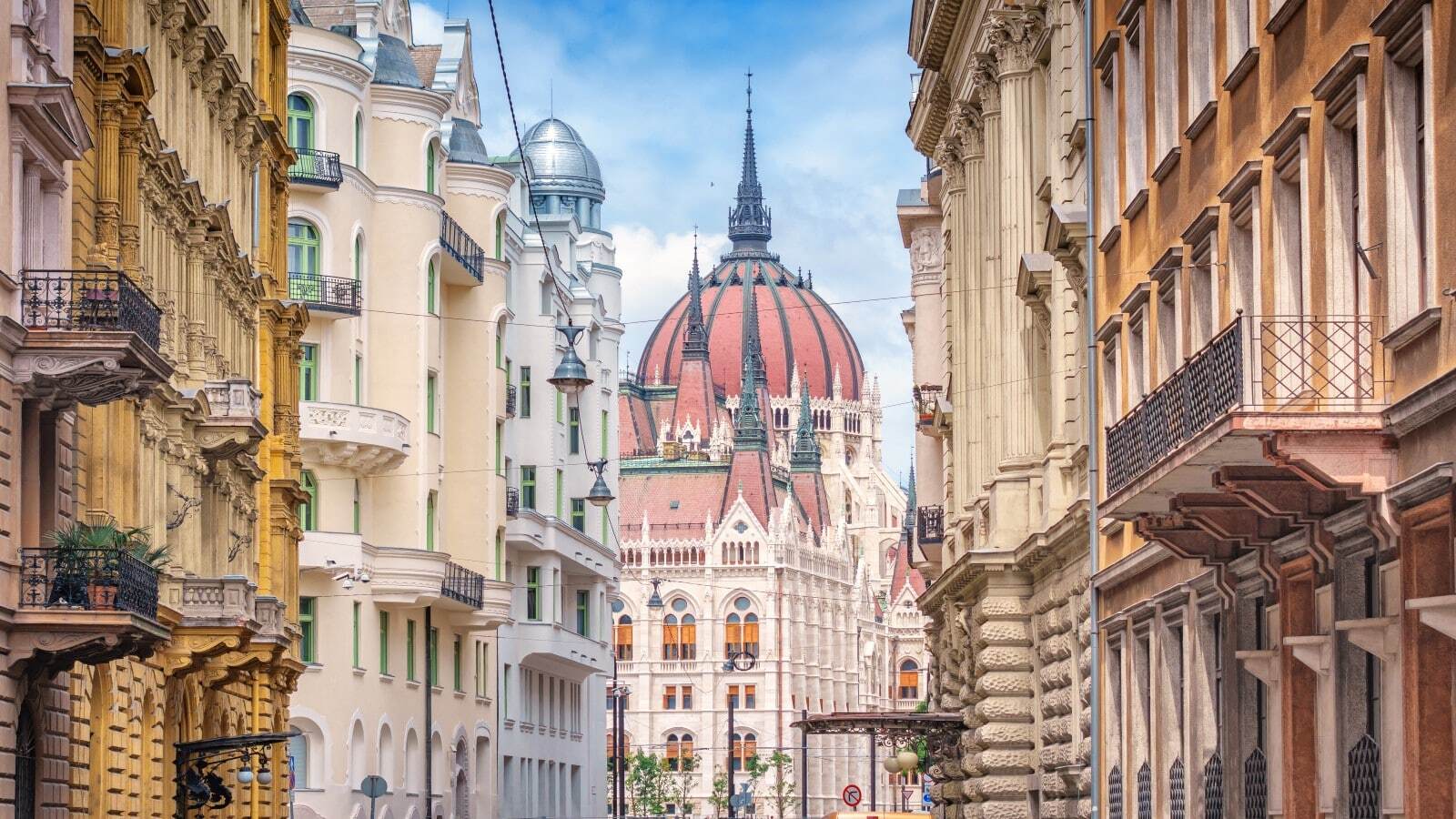 Parliament building and old, ornate apartment buildings in Budapest, Hungary on a sunny day.