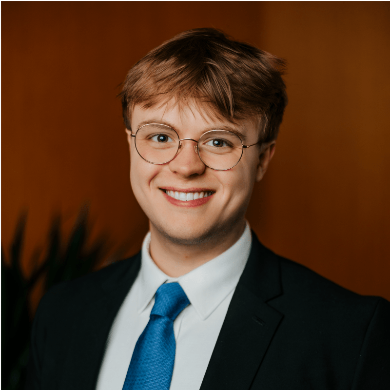 Student wearing a suit, blue tie and jacket in front of orange background