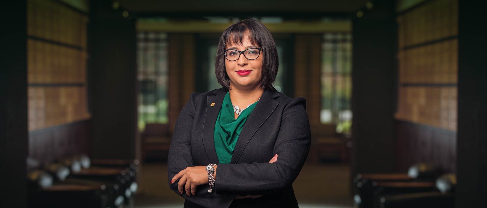 Michigan State Broad College Executive MBA alumnae Carolina Fuentes poses with arms crossed inside the lobby of the Henry Center for Executive Development