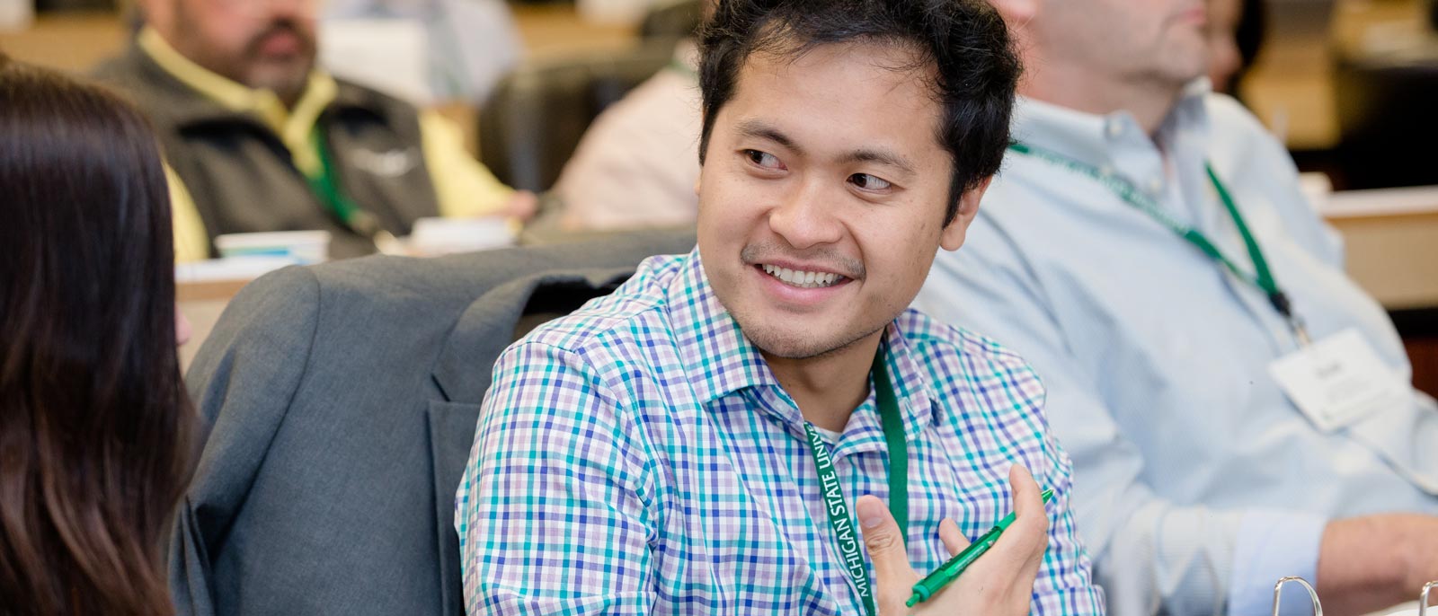 Attendee for supply chain management course at the Henry Center for Executive Development talks with the person next to him in a tiered classroom setting.