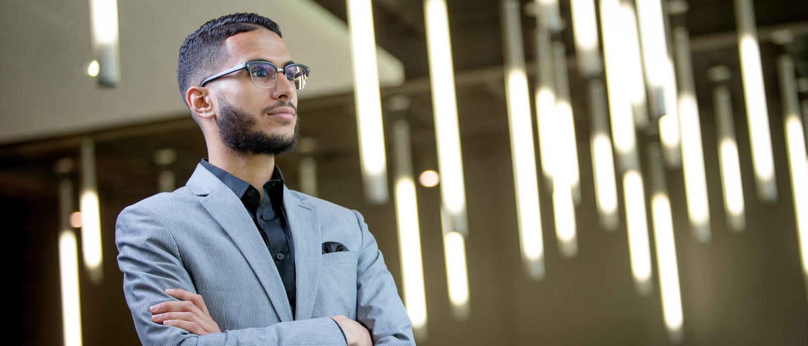 Michigan State Full-Time MBA graduate Mo Hrezi stands against a backdrop of lights with arms crossed.