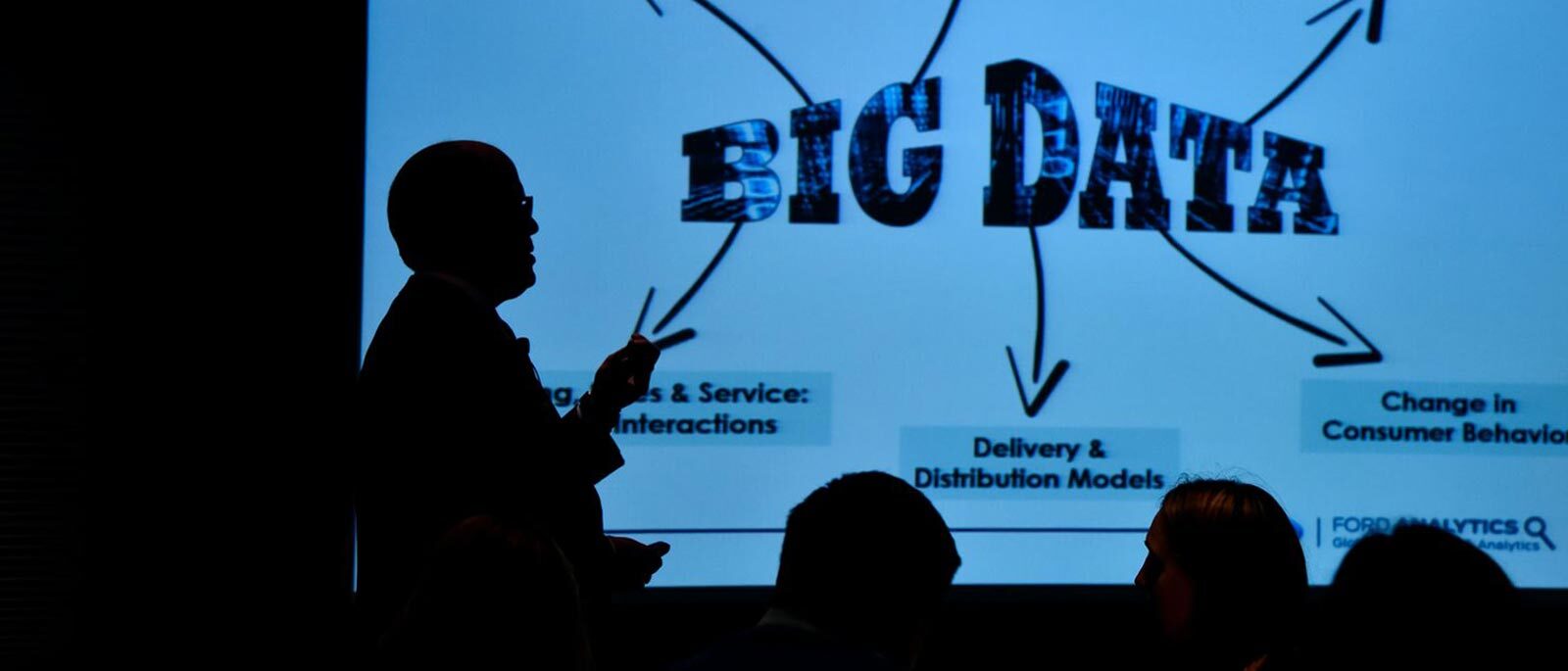 A silhouette of a professor teaching a course on data science in front of the classroom, pointing at a projector screen with 