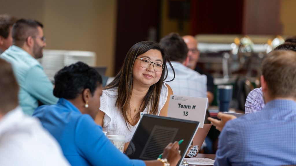 Executive MBA students sit around a table and collaborate at orientation.