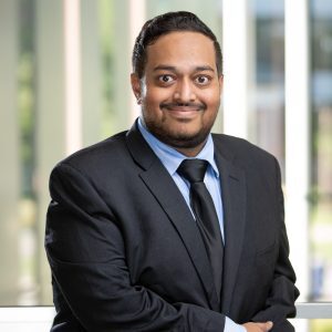 Headshot of Ganesh Shekar, male presenting adult wearing a suit and tie