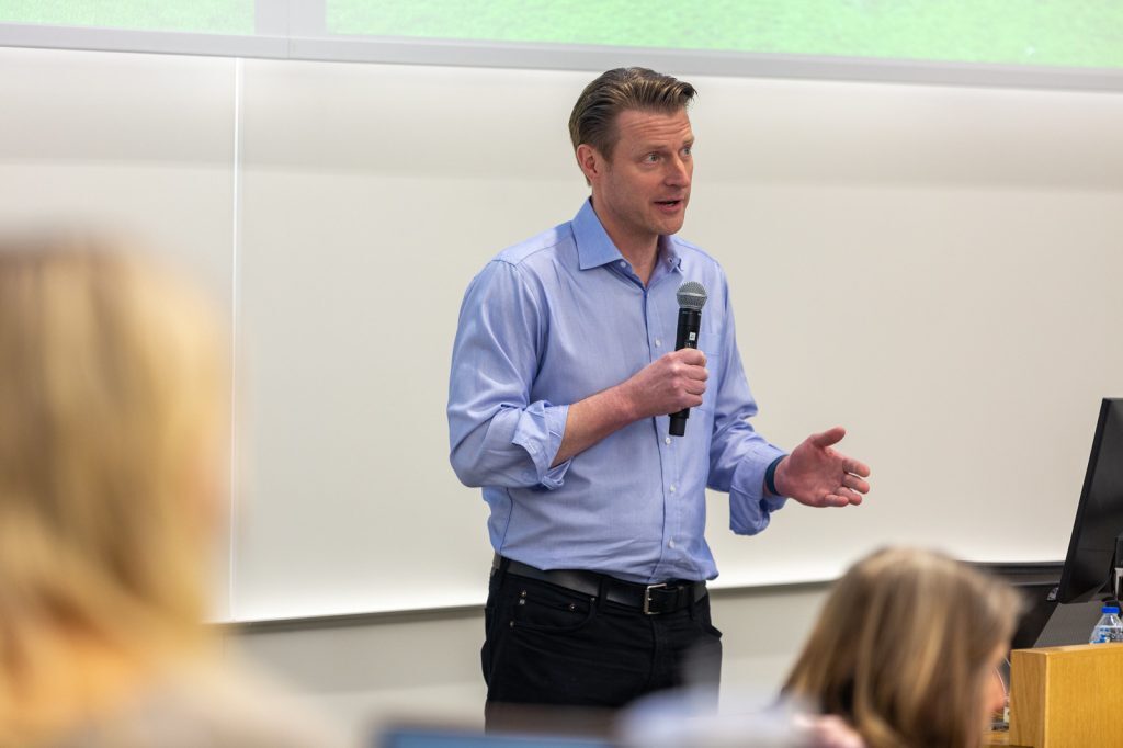 Erik Brown holds a microphone and speaks in an MSU classroom.