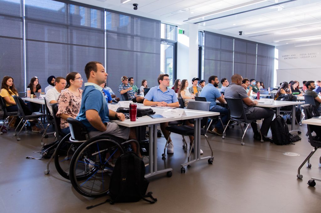 MBA students fill a classroom and listen to a speaker's presentation.