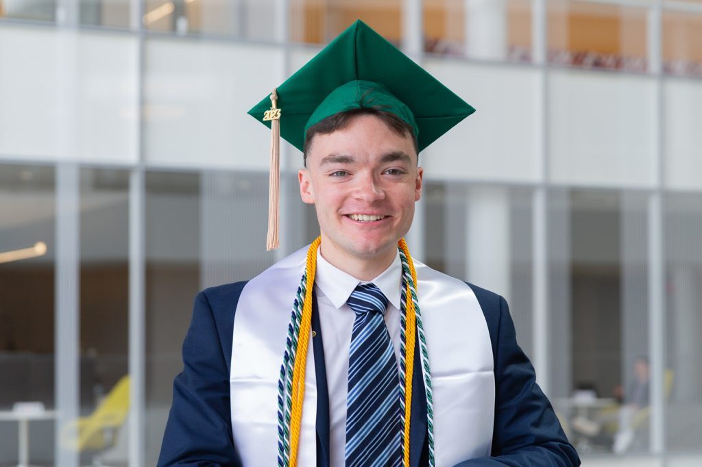 Carlos Conrad poses in the Minskoff Pavilion wearing graduation tassels and cap.