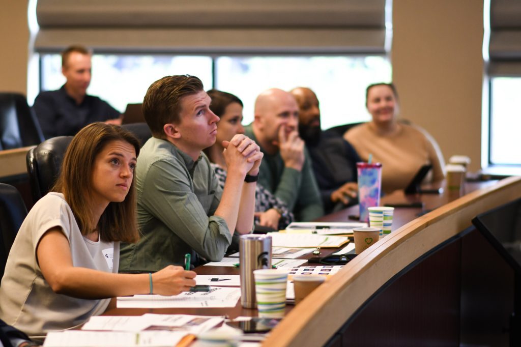 Alumni judges sit and listen to student presentations, while taking notes.