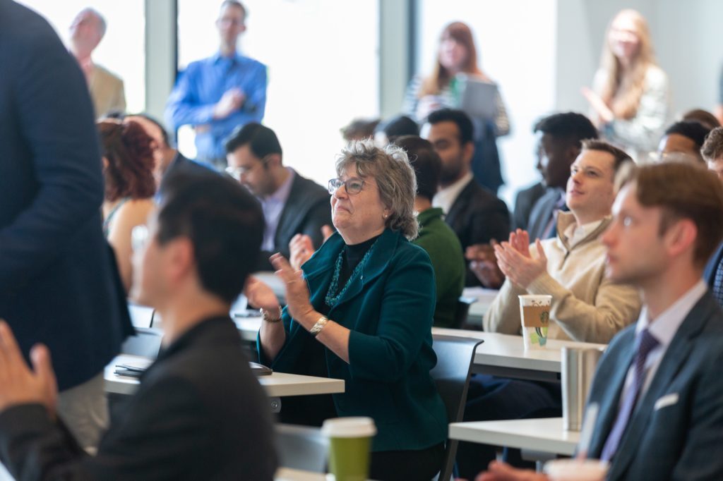Woman sitting in a room of people looking forward and applauding.