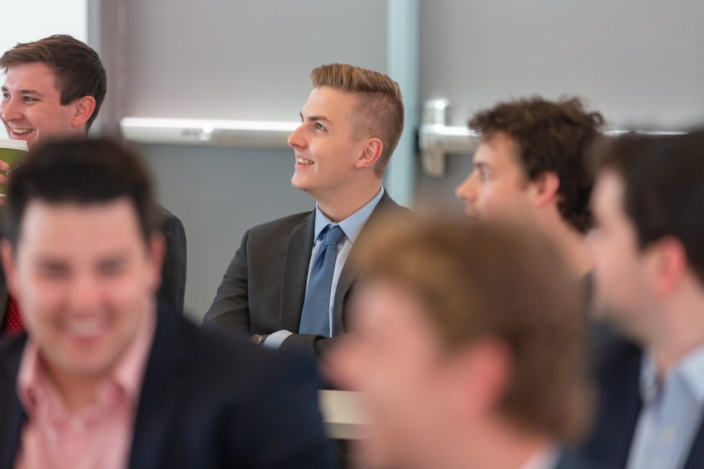 Male students sitting and looking left, listening to a speaker.