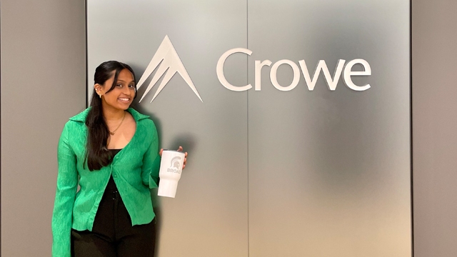 Meg Seetha holding a Broad College tumbler in front of the Crowe logo