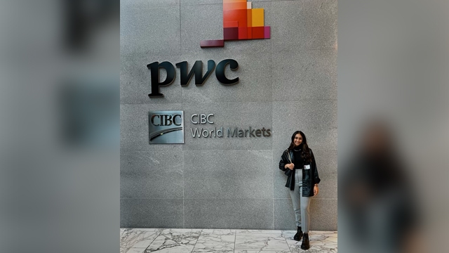 Riya Patel posing in front of the PwC logo