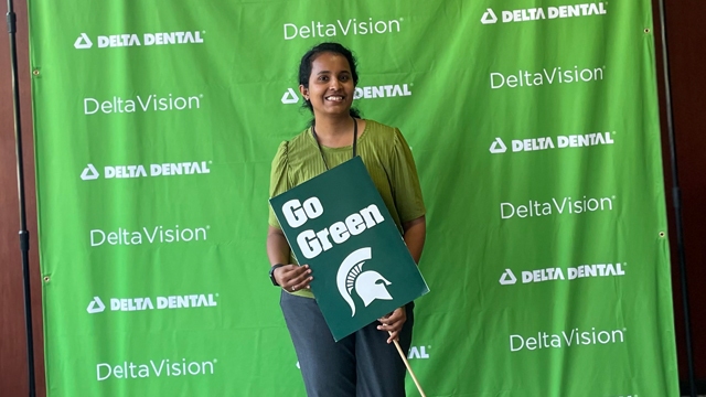 Shri Thaneval holding a "Go Green" sign in front of a Delta Dental backdrop