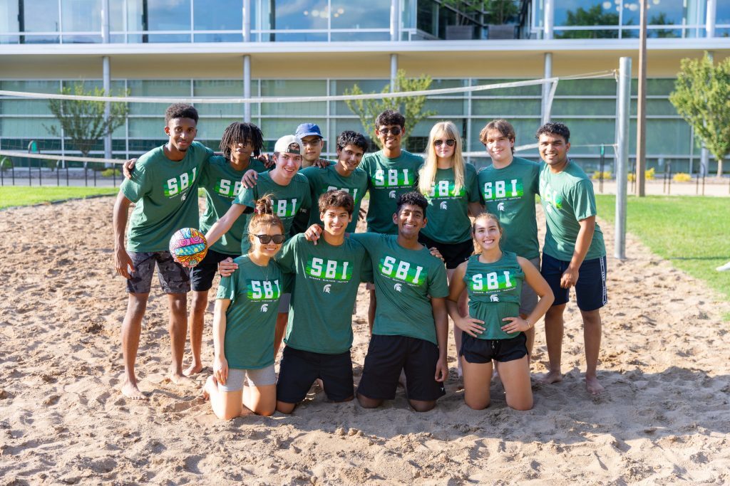 Group photo of students in the Summer Business Institute playing volleyball in the sand