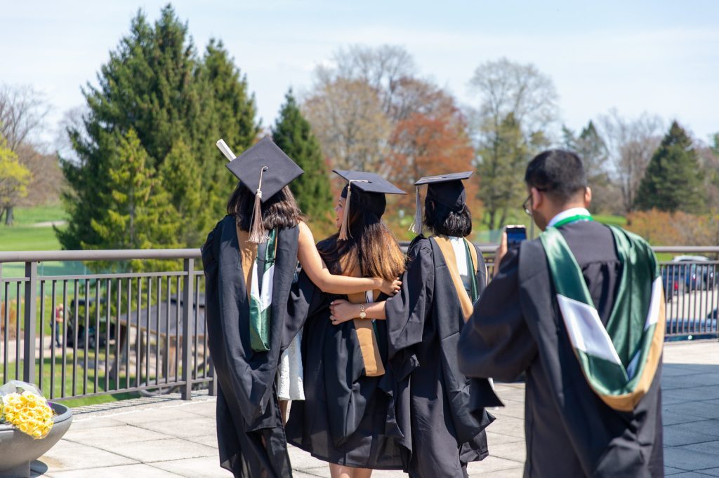 Broad MBA students pose with their backs to the camera on graduation day, wearing academic regalia.