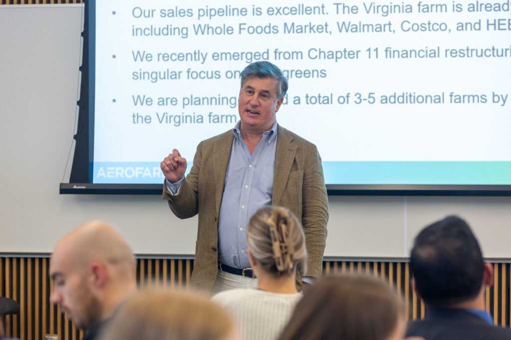 Chris McGraw gestures while speaking in front of a PowerPoint presentation.