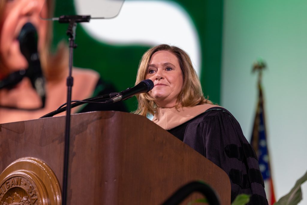 Linda Apsey standing at the MSU Commencement podium, delivering her address.
