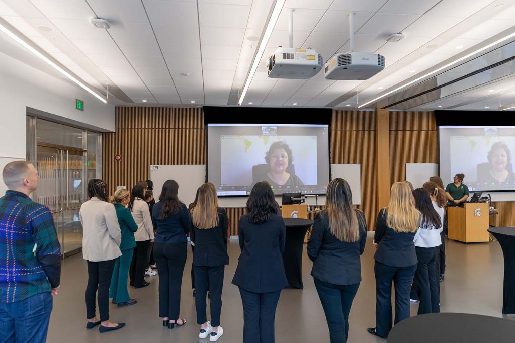 DWLA Scholars, Broad faculty and staff fill the Entrepreneurship Lab in the Minskoff Pavilion. Priya Balasubramanium is seen via Zoom projected on a presentation screen in the room.