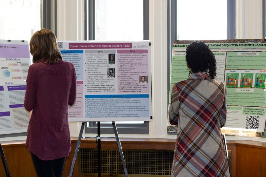 Two people facing away from camera standing and reading research posters at the 2024 Diversity Research Showcase.