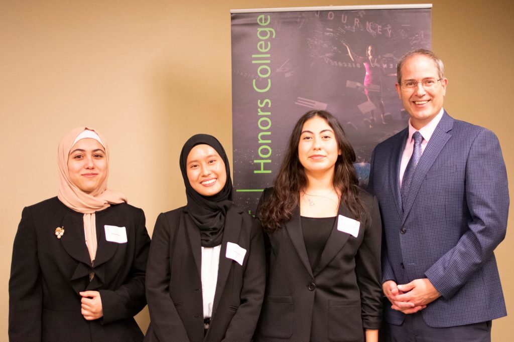 Three students pose with Chris Long after presenting their winning work on classroom implications of AI plagiarism and fabrication.