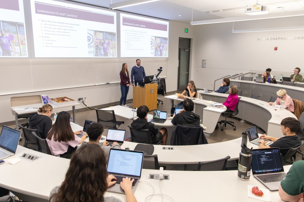 Tiered classroom as seen from back of the class, Andrew and Monica Gauthier standing and presenting.