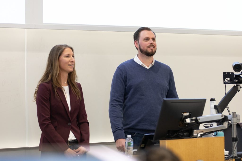 Monica and Andrew Gauthier stand in front of a compute and podium while speaking to a class of Spartans.