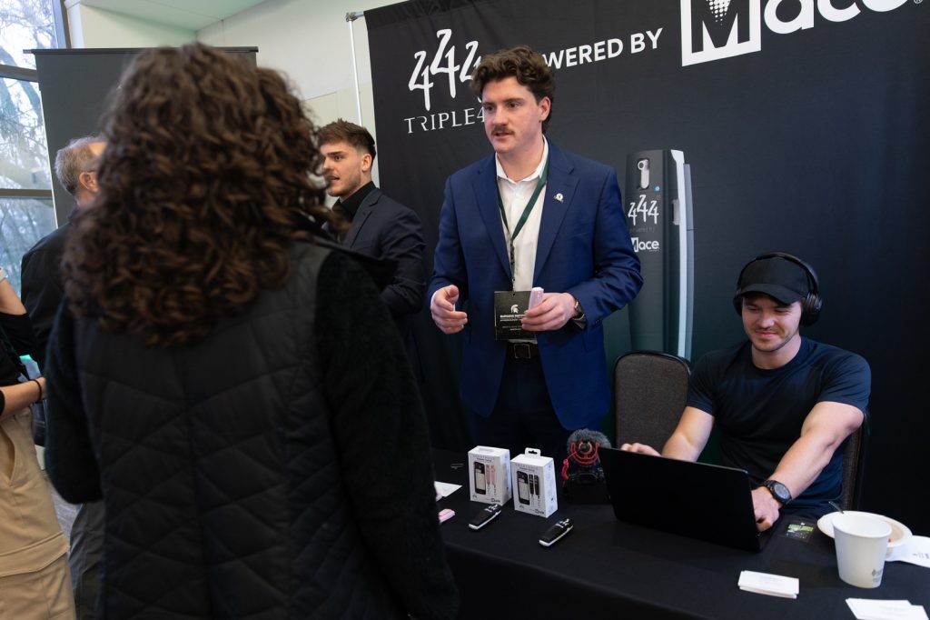 Spartan entrepreneurs stand behind a table with branded materials, talking with Burgess New Venture Challenge attendees.