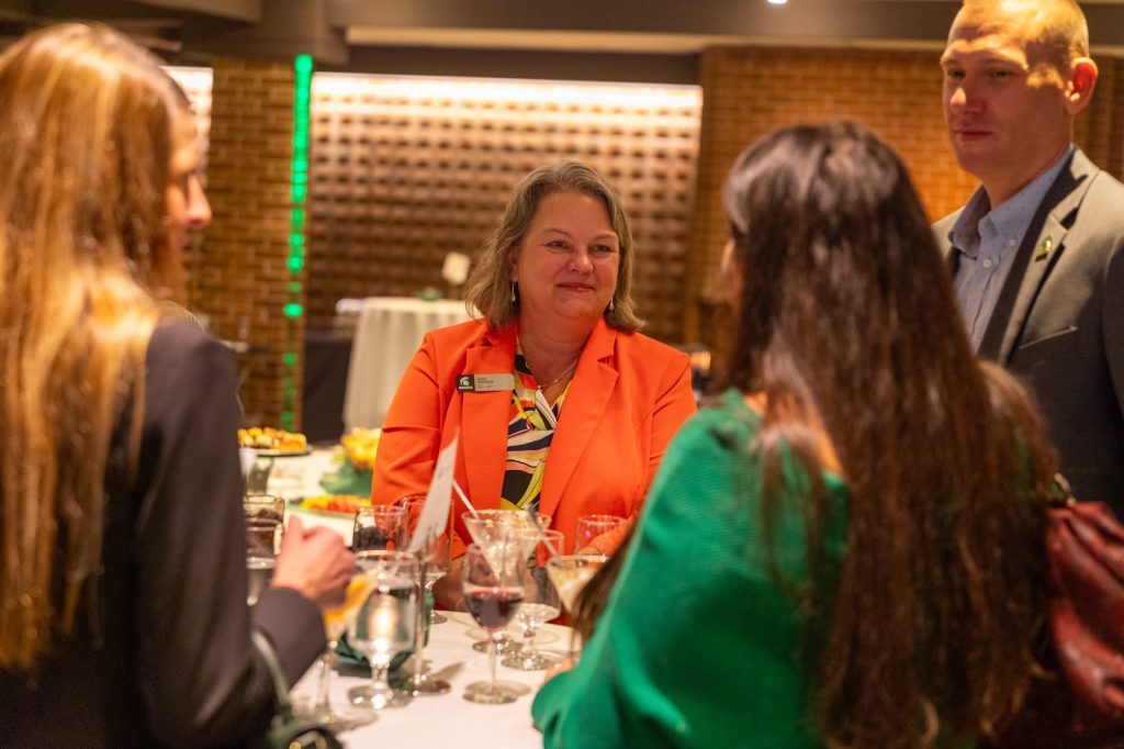 Judith Whipple stands at a high-top table and networks with Broad staff, alumni and students at a college event.