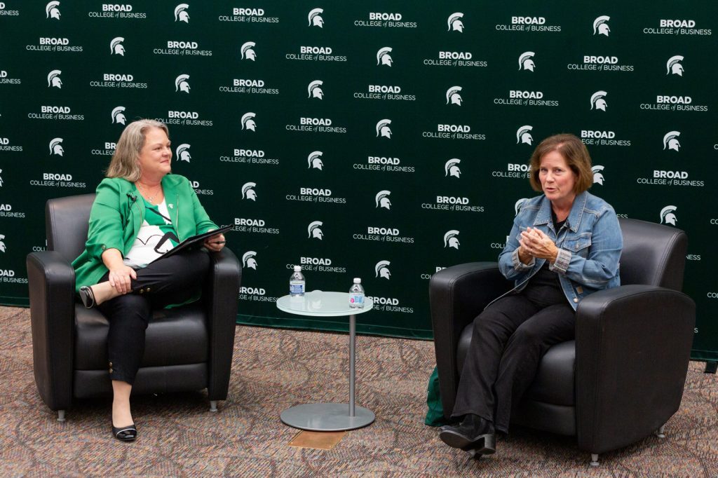 Judith Whipple and Linda Hubbard sit in executive chairs and speak at the 2023 Warrington Lecture.