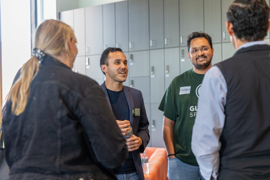 A group of Broad students, alumni and staff stand in a group and talk in the Minskoff Pavilion.