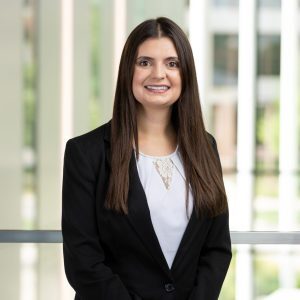 young, feminine presenting woman with light skin and long, straight brown hair smiling and posing in business attire.