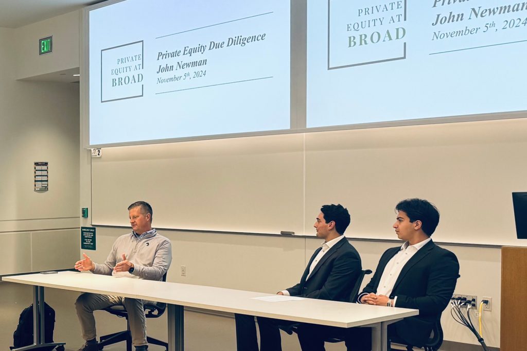 Three people sitting at table with projection behind them