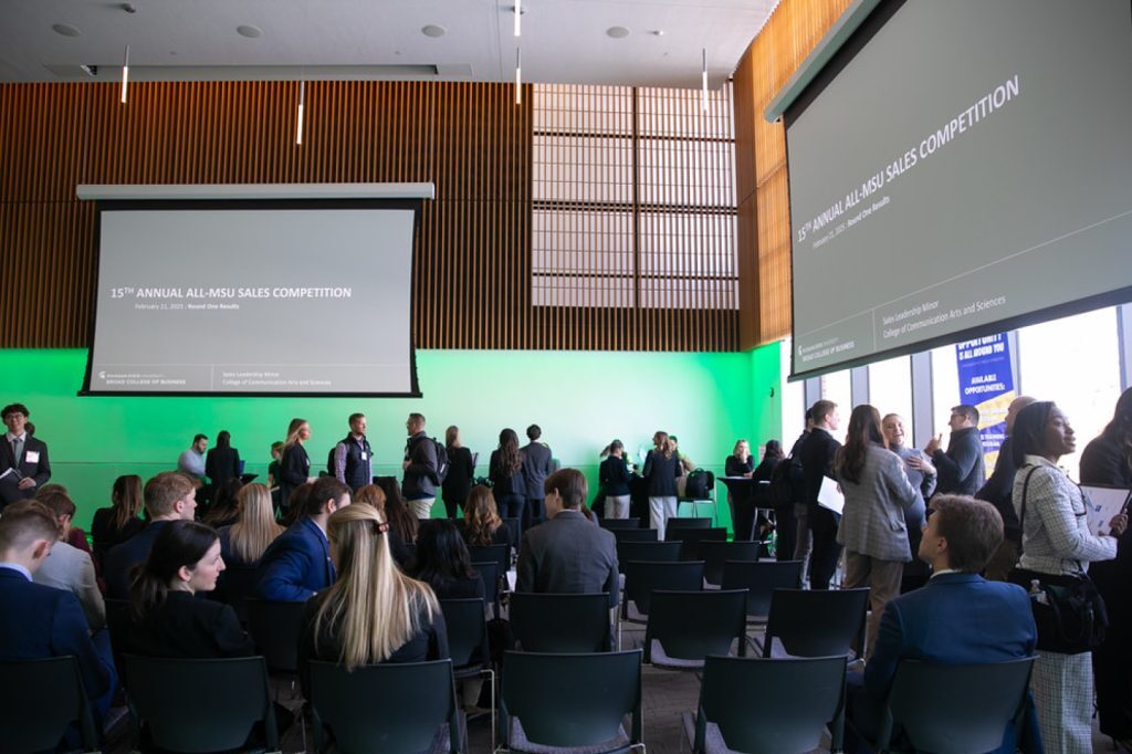 Group of participants in conference room with event information on projector screens