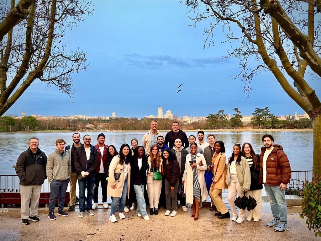 photo of several adults in a group with blue sky and water in the background, and a tree on either side of the group.