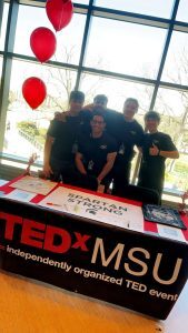 Group photo at the TEDxMSU event table.