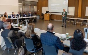 A person stands in front of a group of people sitting at tables facing him