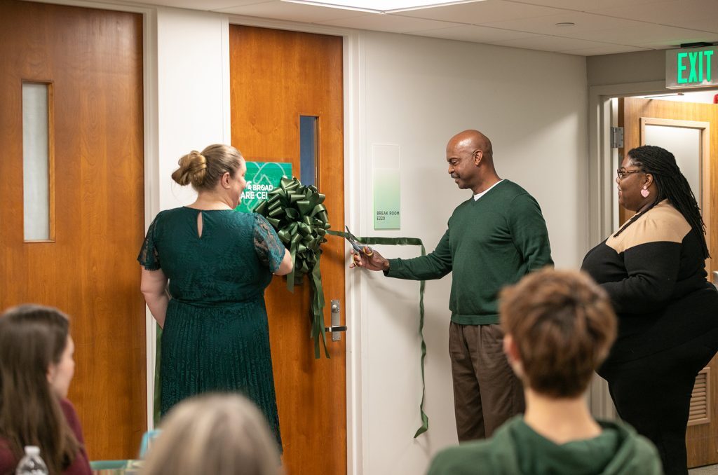 Two people cutting a green ribbon on a door