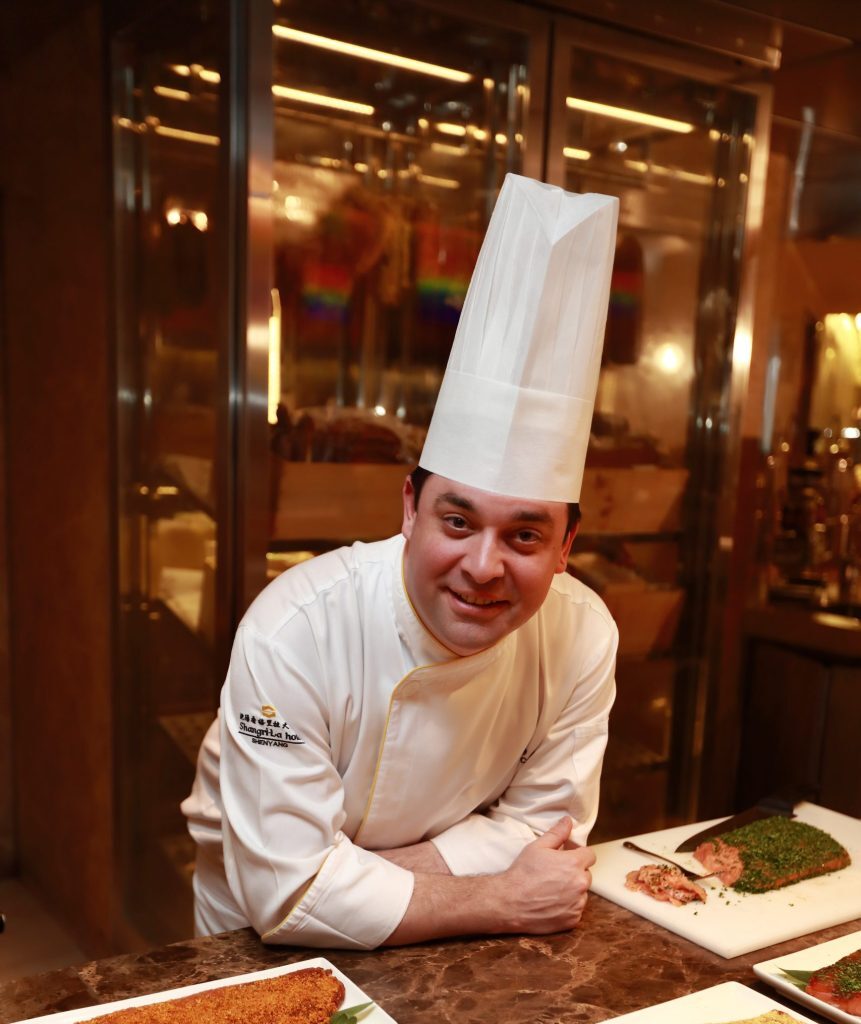 Chef leaning on table with plated food smiling at the table