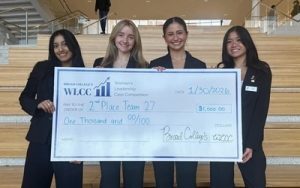 Vivian Tieu, Megan Howarth, Sofia Poulos and Anvi Thakur stand at the bottom of a stair case holding a large check.