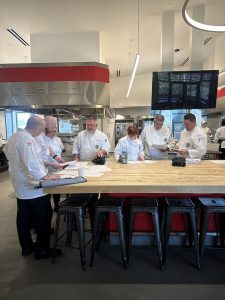 Chefs standing around work table and listening to demonstration 
