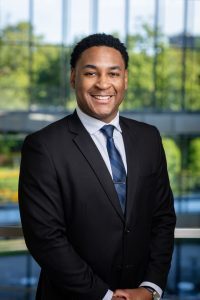 headshot of a smiling man with dark skin and dark hair wearing a business suit