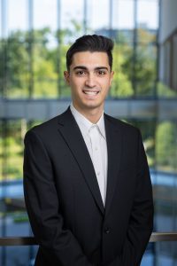 headshot of a smiling man with light skin and dark hair wearing a business suit 
