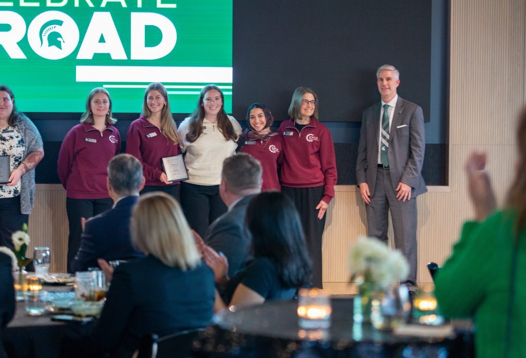 A group of students stands on stage holding an award plaque as attendees applaud during the Celebrate Broad ceremony.