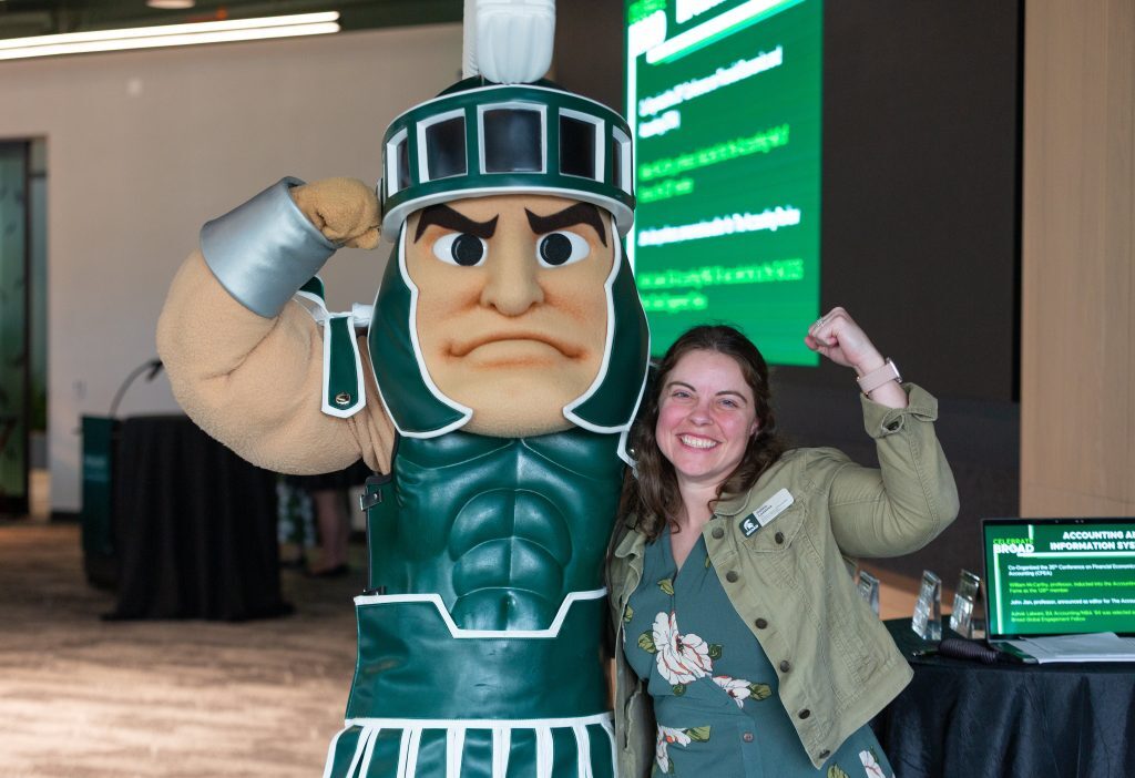 A smiling attendee poses flexing alongside the Michigan State Spartan mascot during the event.