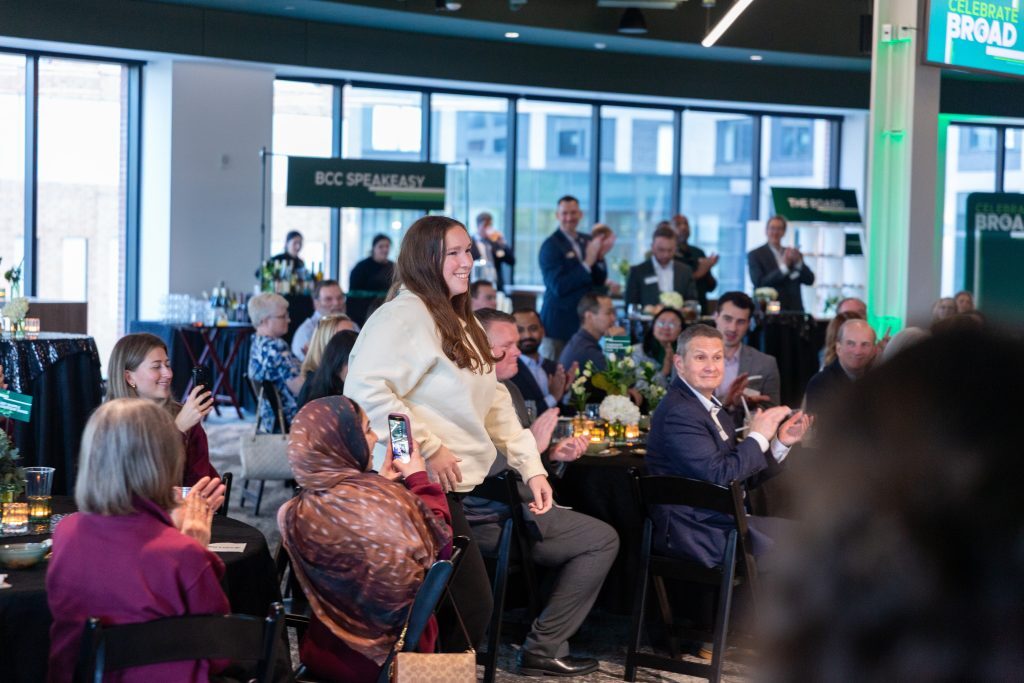A student walks through the audience smiling as attendees applaud during the Celebrate Broad event.