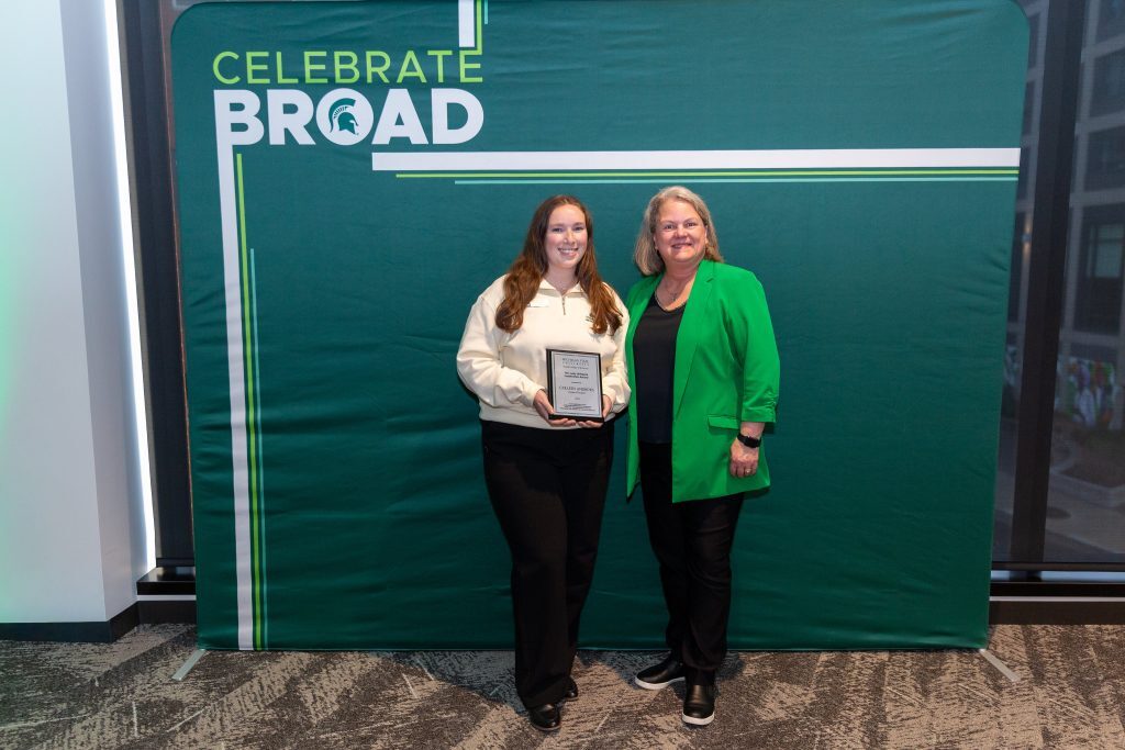 A student award recipient poses with a plaque alongside another attendee in front of a “Celebrate Broad” backdrop.