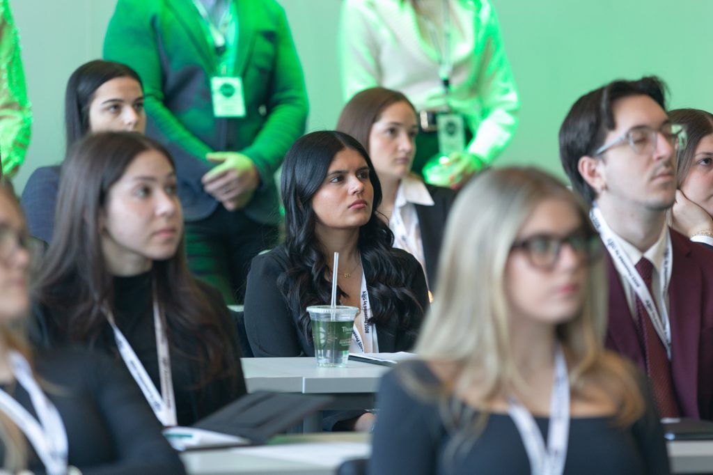 Close-up of students in business attire listening attentively during a presentation, seated at classroom tables with notebooks and drinks.
